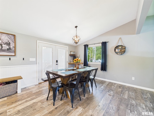 dining area with a notable chandelier, light wood-style floors, french doors, and lofted ceiling