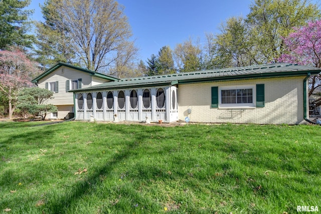 back of house featuring brick siding, a yard, and a sunroom