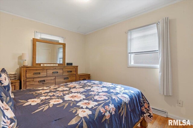 bedroom with a baseboard radiator, wood finished floors, ornamental molding, and baseboards