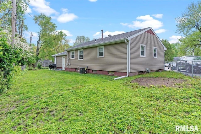 rear view of house featuring fence, central AC unit, and a lawn