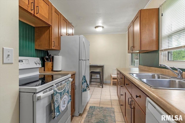kitchen with a sink, light tile patterned flooring, white appliances, brown cabinetry, and light countertops