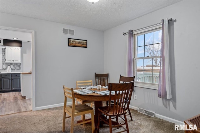 dining space with baseboards, visible vents, light carpet, and a textured ceiling