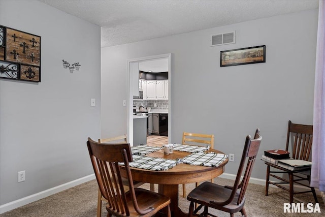 dining space with a textured ceiling, visible vents, light colored carpet, and baseboards