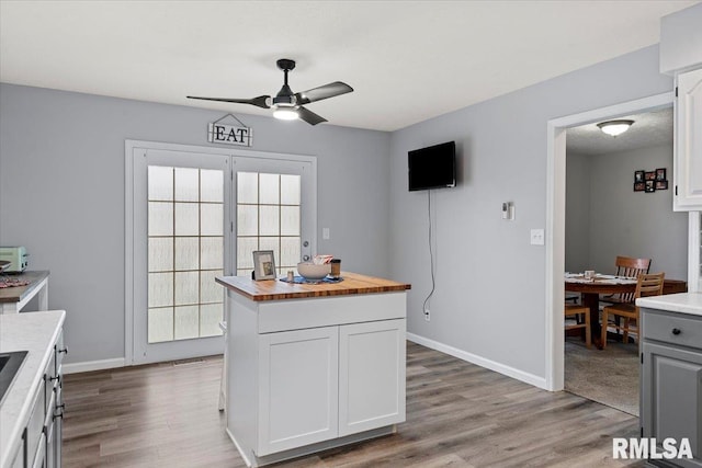 kitchen featuring white cabinets, wood finished floors, a ceiling fan, and butcher block countertops