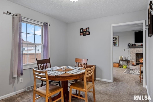 carpeted dining room featuring a fireplace, a textured ceiling, a healthy amount of sunlight, and baseboards