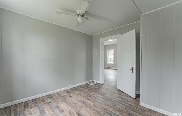 empty room with wood finished floors, ornamental molding, ceiling fan, baseboards, and visible vents