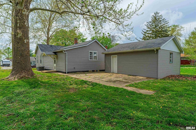 rear view of house with an outbuilding, a lawn, a patio, and central AC unit