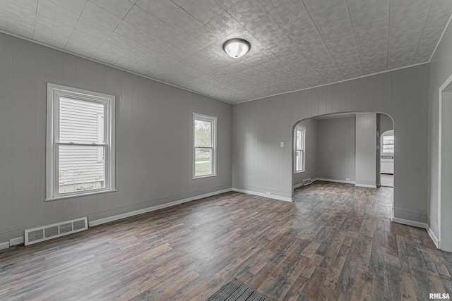 unfurnished room with baseboards, visible vents, arched walkways, and dark wood-style flooring