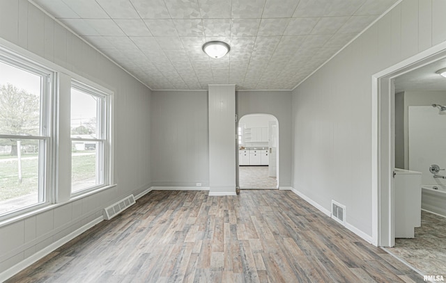 empty room featuring wood finished floors, visible vents, and arched walkways