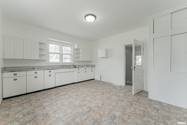 kitchen featuring stainless steel counters, open shelves, white cabinets, a sink, and stone finish flooring