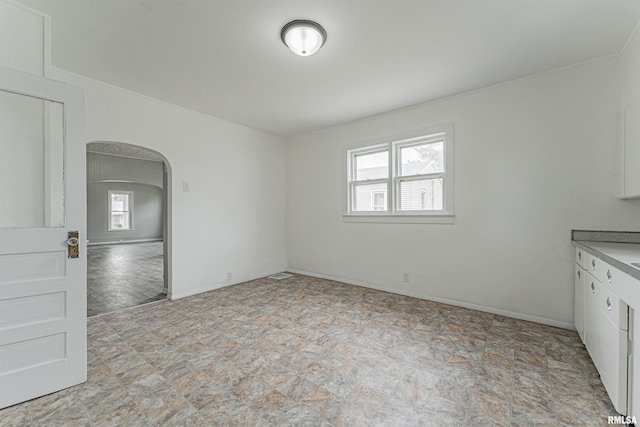 unfurnished dining area with arched walkways, stone finish floor, and a wealth of natural light