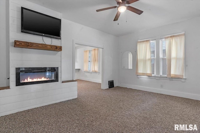 unfurnished living room featuring a glass covered fireplace, baseboards, ceiling fan, and carpet