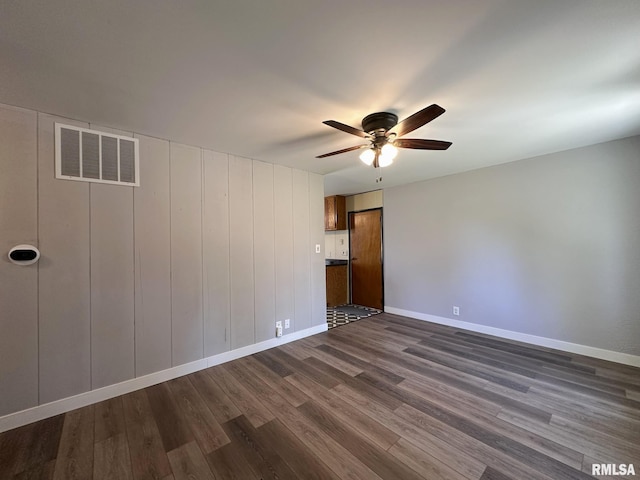 empty room with baseboards, a ceiling fan, dark wood-style flooring, and visible vents