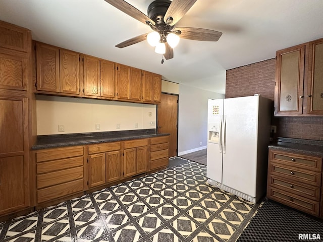 kitchen with dark countertops, white refrigerator with ice dispenser, and brown cabinetry