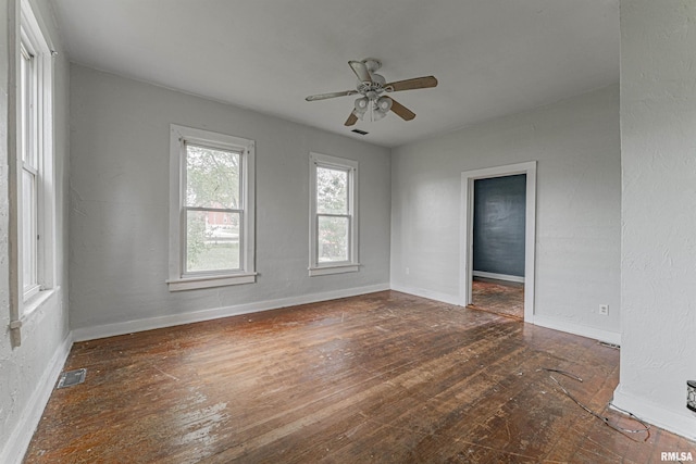 empty room with wood-type flooring, a ceiling fan, baseboards, and visible vents
