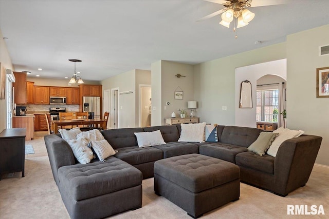 living room featuring light colored carpet, arched walkways, ceiling fan, and visible vents