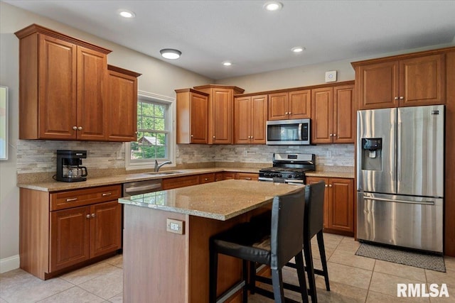 kitchen with a sink, appliances with stainless steel finishes, brown cabinets, and light tile patterned flooring