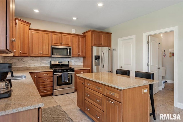 kitchen featuring a breakfast bar area, light tile patterned flooring, appliances with stainless steel finishes, and brown cabinetry