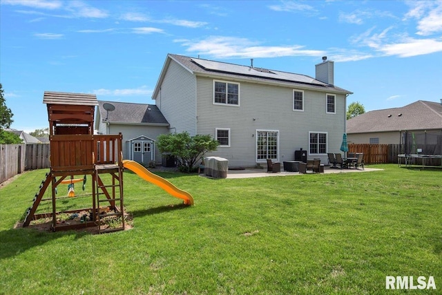 back of property featuring a fenced backyard, a chimney, a patio area, a trampoline, and solar panels