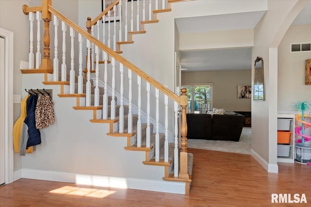 stairs with arched walkways, baseboards, visible vents, and wood finished floors