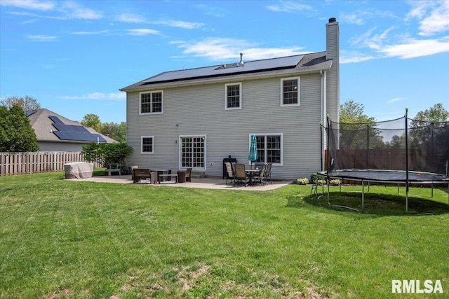 back of house featuring roof mounted solar panels, a trampoline, a yard, and a patio area