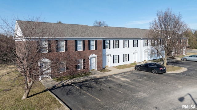colonial-style house with roof with shingles and uncovered parking