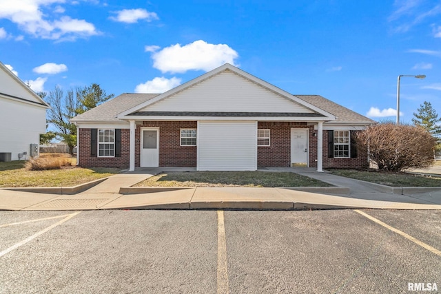 view of front of house featuring brick siding, central AC unit, and uncovered parking