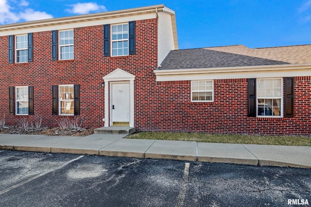 colonial-style house featuring brick siding, a shingled roof, and uncovered parking