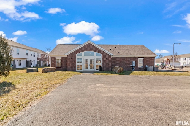 view of front of home featuring a front yard, french doors, brick siding, a playground, and central air condition unit