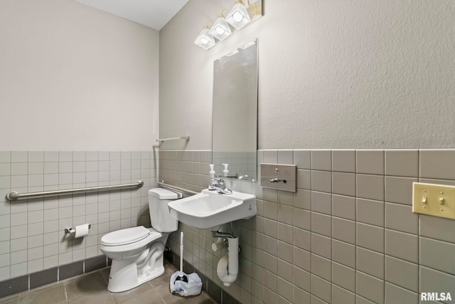 bathroom with tile walls, a sink, tile patterned floors, a wainscoted wall, and toilet
