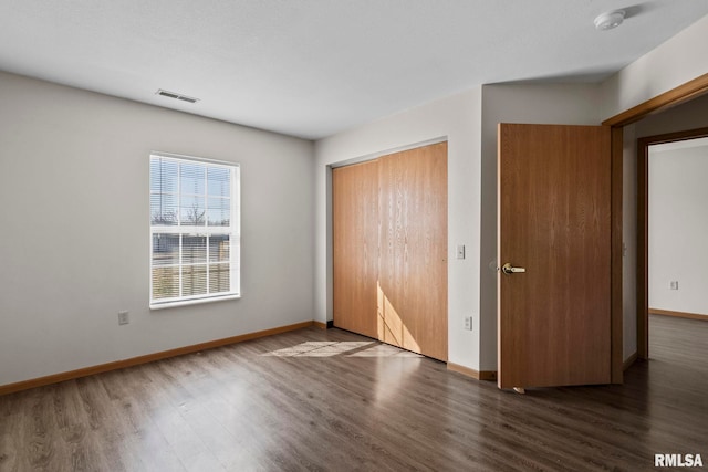 unfurnished bedroom with baseboards, visible vents, wood finished floors, and a closet