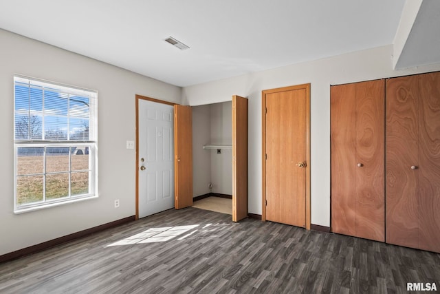 unfurnished bedroom featuring baseboards, two closets, wood finished floors, and visible vents