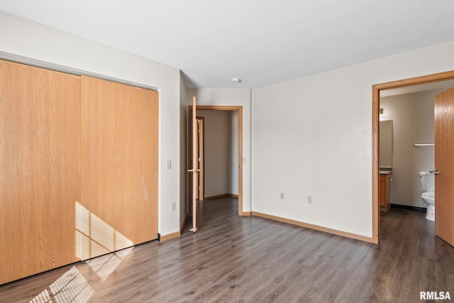 unfurnished bedroom featuring baseboards, ensuite bathroom, a closet, and wood finished floors