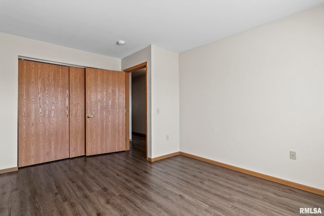 unfurnished bedroom with a closet, baseboards, and dark wood-type flooring