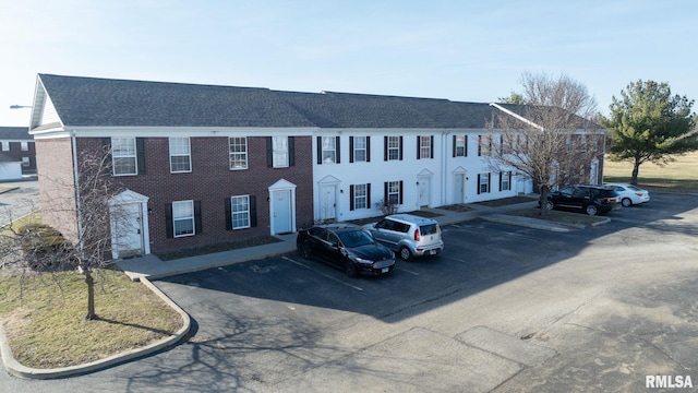 view of front of property with brick siding, uncovered parking, and roof with shingles