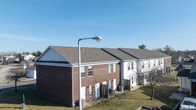 view of side of property featuring brick siding, a lawn, roof with shingles, and a residential view