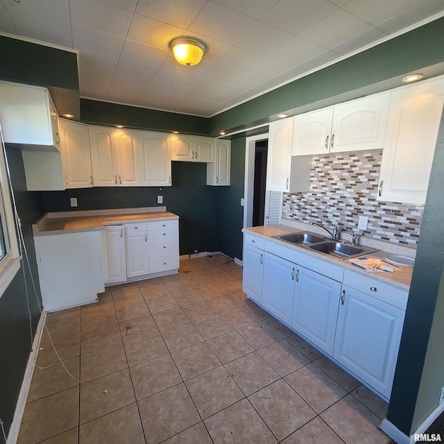 kitchen with decorative backsplash, a sink, tile patterned floors, baseboards, and white cabinetry