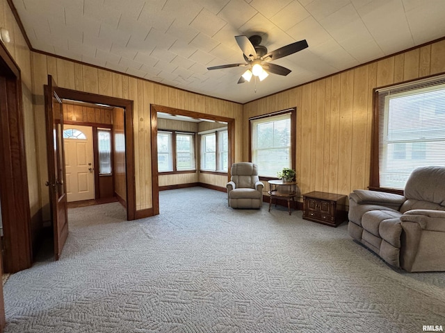 living room with crown molding, carpet, a ceiling fan, and wood walls