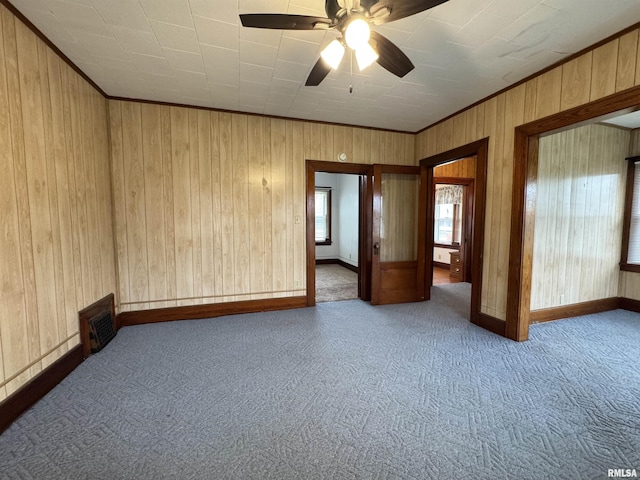 empty room with crown molding, visible vents, wood walls, ceiling fan, and carpet flooring