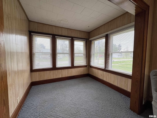 unfurnished sunroom with baseboards, carpet flooring, and wood walls