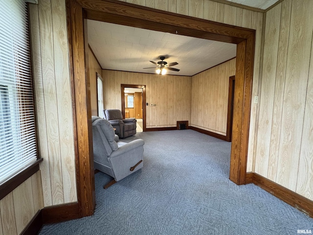 sitting room with baseboards, carpet flooring, ceiling fan, and wooden walls