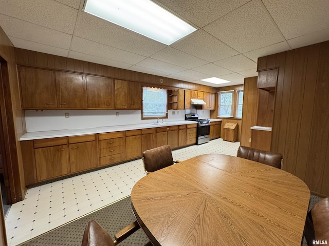 kitchen featuring open shelves, a sink, gas stove, wood walls, and under cabinet range hood
