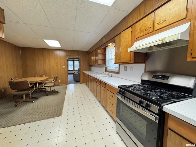 kitchen with brown cabinets, open shelves, a sink, gas stove, and under cabinet range hood