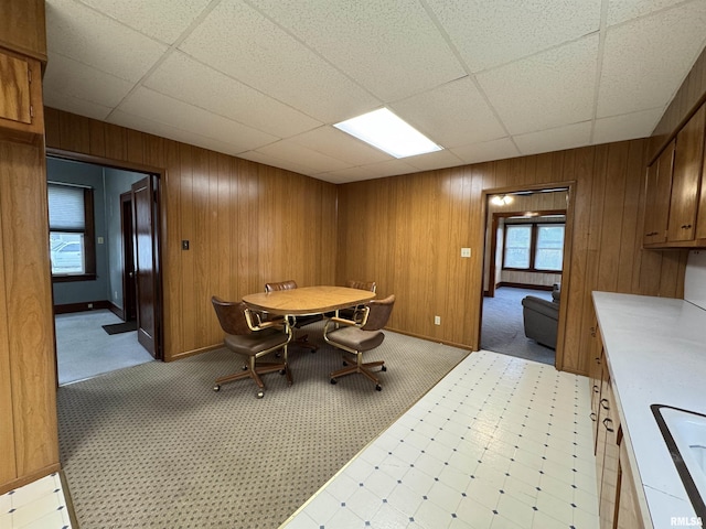 dining space with wood walls, a drop ceiling, and light carpet