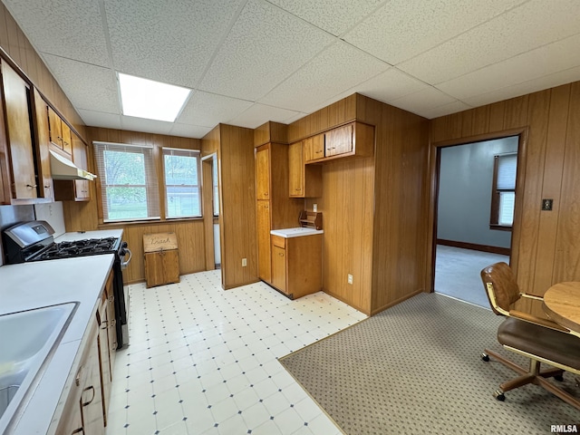 kitchen with light countertops, under cabinet range hood, brown cabinets, range with gas cooktop, and a sink