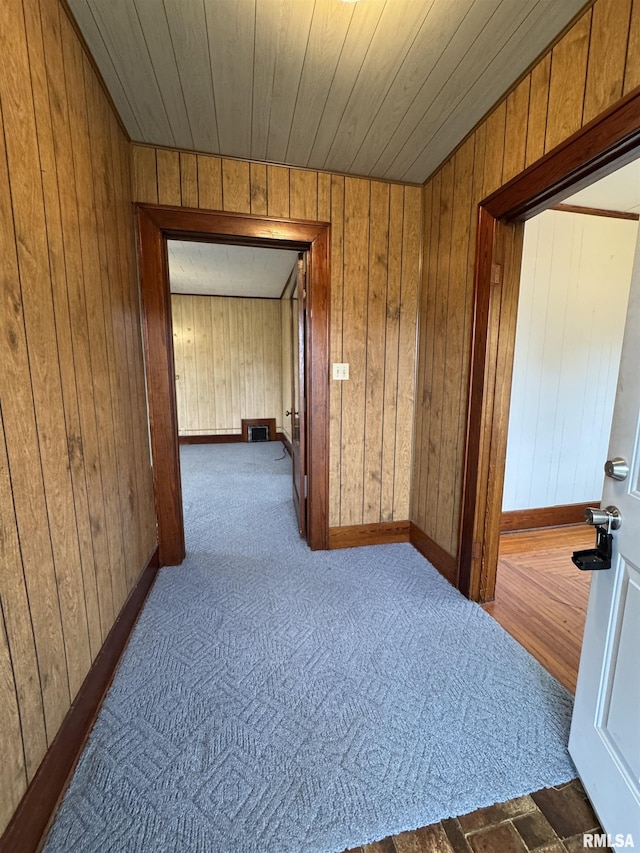 hall featuring baseboards, carpet, wood ceiling, and wood walls