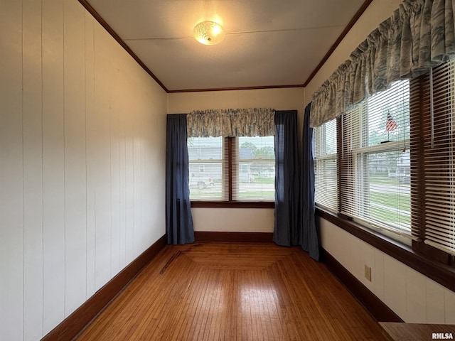 unfurnished room with crown molding, baseboards, wood walls, and a wealth of natural light