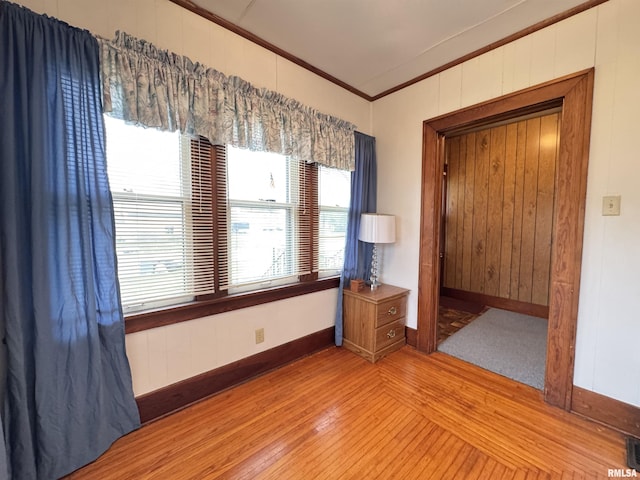 empty room with visible vents, crown molding, wood walls, baseboards, and light wood finished floors