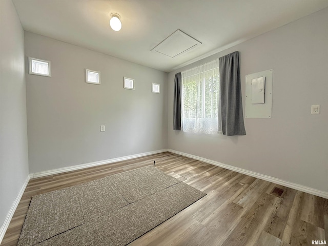 spare room featuring baseboards, electric panel, wood finished floors, and visible vents
