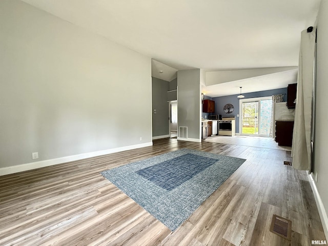 unfurnished living room with baseboards, visible vents, wood finished floors, and lofted ceiling